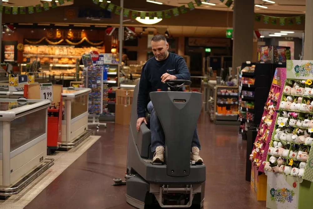 Mitarbeiter der Total Reinigung auf einer Aufsitz-Scheuersaugmaschine im Supermarkt